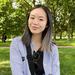 Victoria Tan has shoulder length hair, wearing a blue and white top and is sitting in a park.