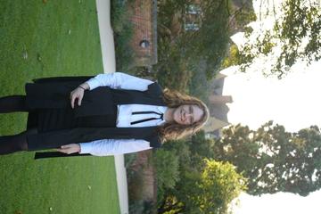 Matriculation Nicola is have brown/redish shoulder length hair, is wearing a graduation gown with glasses and smiling at the camera.