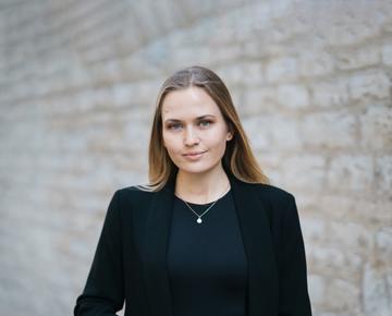 Moa Schafer has shoulder length blond hair, wearing a dark jacket looking at the camera. 