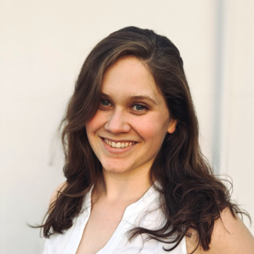 Anja is smiling widely at the camera. She has long dark hair and is wearing a sleeveless white blouse. 