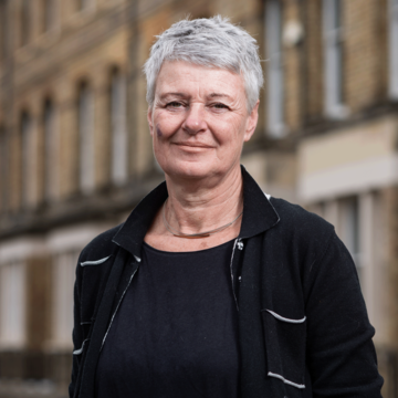 Jane barlow is wearing a black top and jacket, with short gray hair, smiling for the camera.