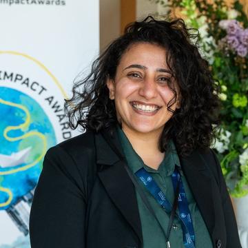 Dr Mona Ibrahim Dr Mona Ibrahim has shoulder-length curly black hair. She is smiling broadly, wearing a dark green blouse and black blazer.