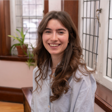 cloe gosselina has brown shoulder length hair, wearing a white and blue stripped top smiling at the camera.