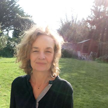 Elaine Chase has short blonde hair and is wearing a black top. She is standing in a grassy area.