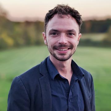 Hal Cooper, with short brown hair, is wearing a dark blue shirt and jacket, smiling at the camera