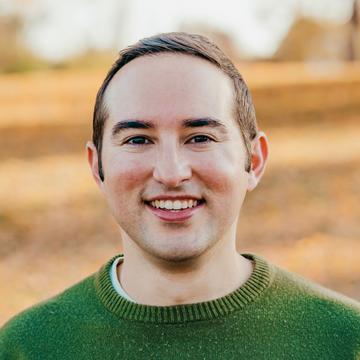 Paul Penahas short brown hair, wearing a green top smiling at the camera.